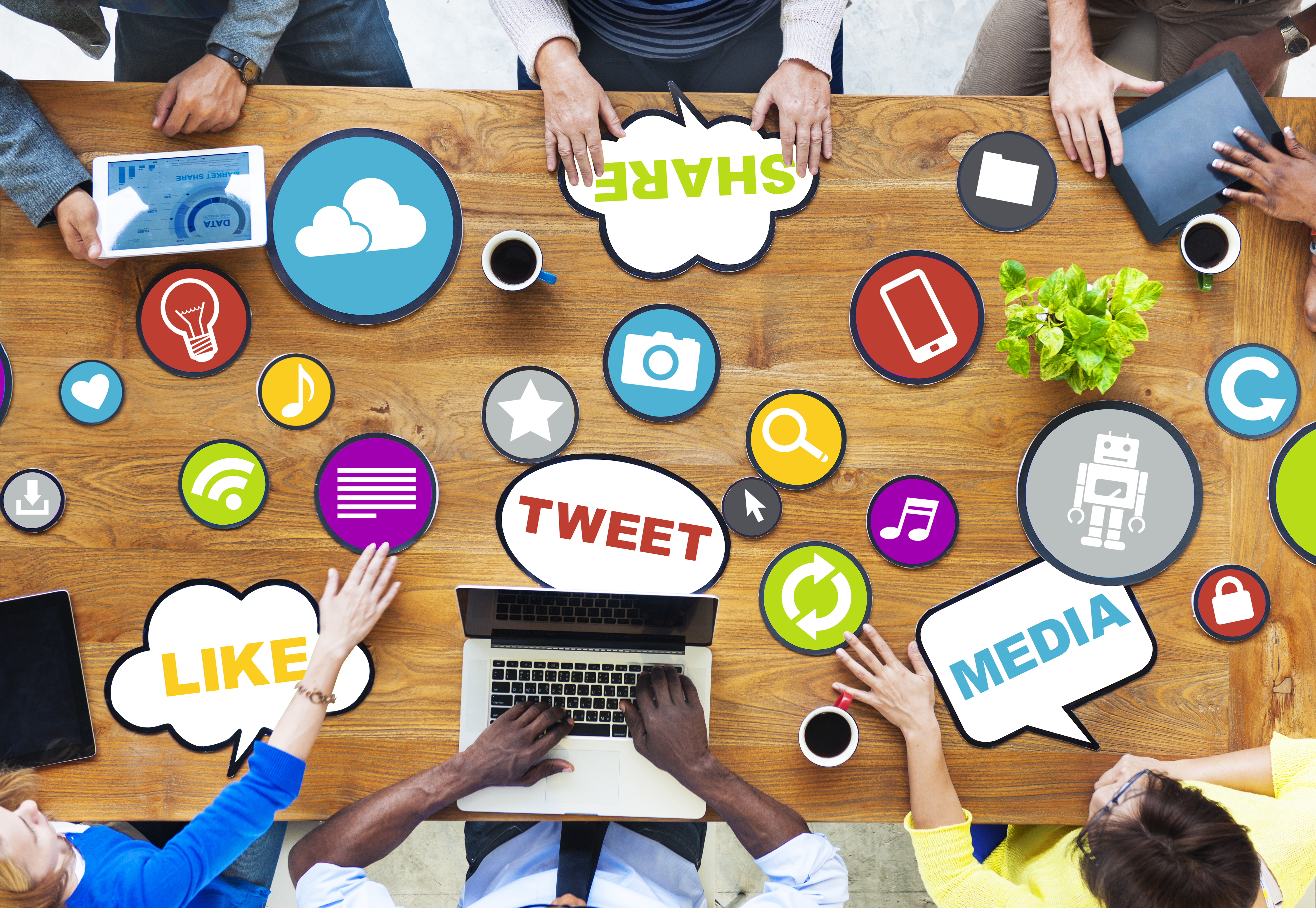 People, laptops, phones, and tablets on table with social sharing icons.